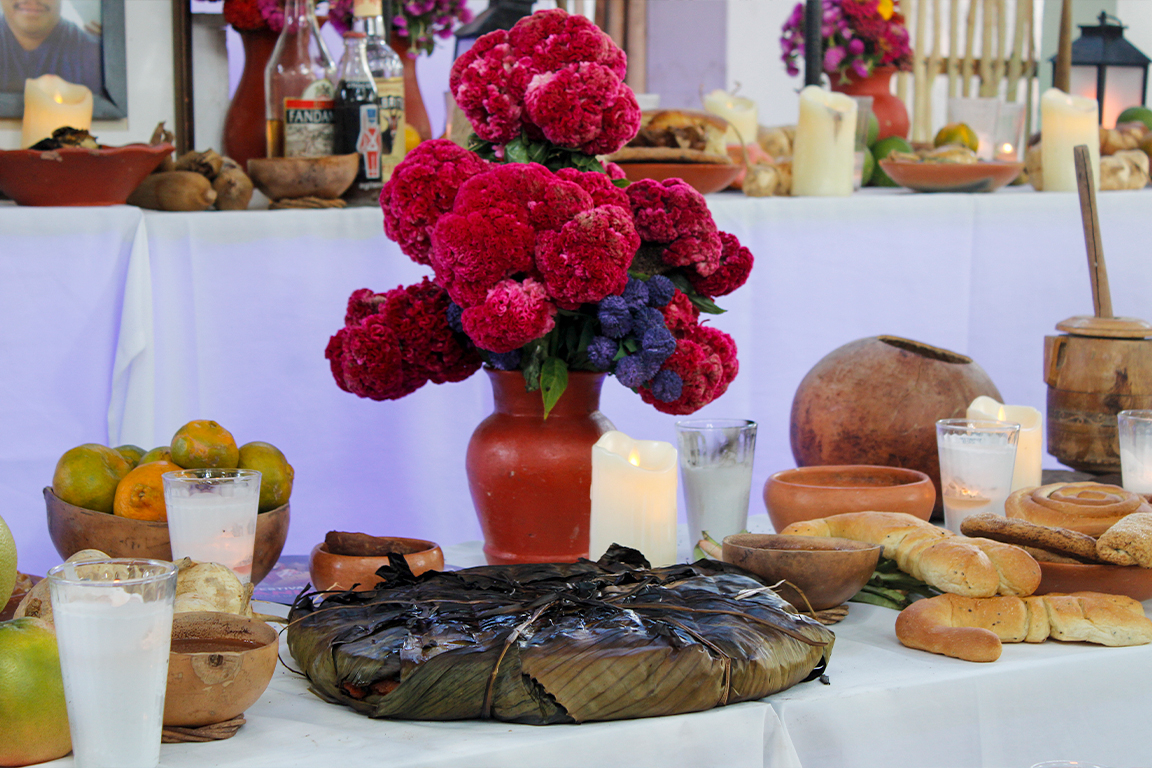 Altar de Hanal Pixán con elementos como el mucbipollo, jícaras, velas y flores.