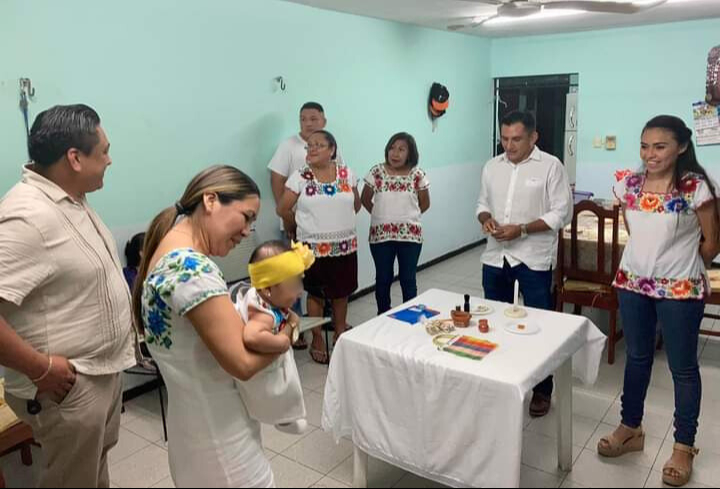 El padrino y la madrina dan nueve vueltas alrededor de la mesa, entregando al niño objetos simbólicos que representan sus futuras habilidades