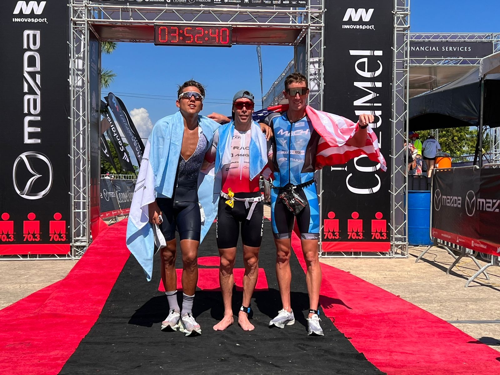 Los atletas que ocuparon los tres primeros lugares del Ironman de Cozumel se fotografiaron con sus respectivas banderas